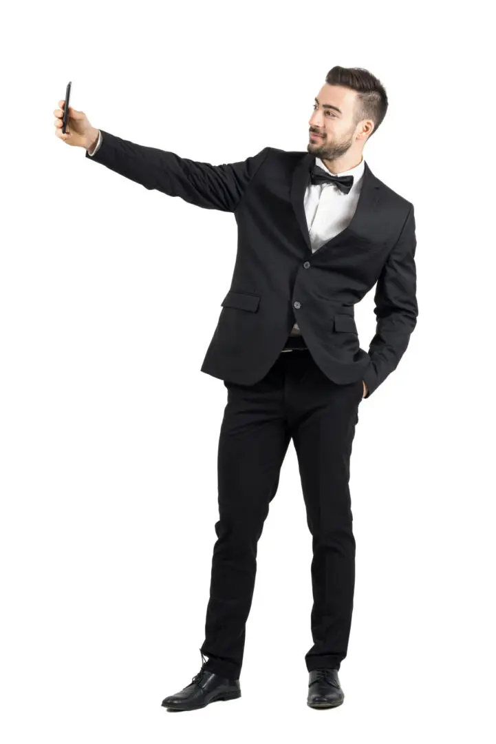 A man in a black tux taking a selfie