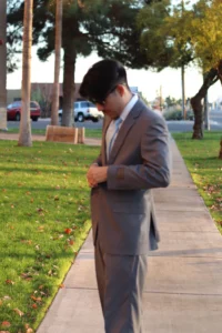 Man Wearing A Grey Suit And Light Blue Tie Walking Outdoors In Phoenix, Perfect For A Semi-Formal Wedding Guest.