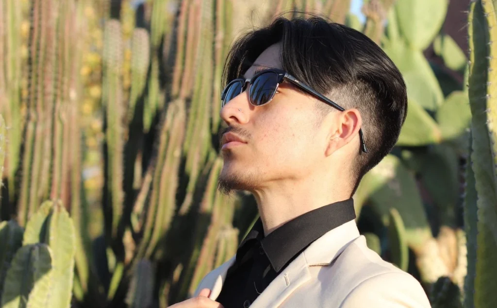 Close Up Of A Man Wearing A Beige Suit With A Black Shirt And Sunglasses In Front Of Desert Cacti In Phoenix.