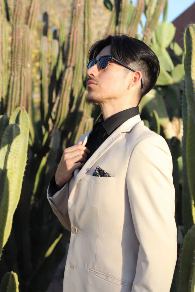 Man Wearing A Beige Suit With Black Shirt And Sunglasses Standing In Front Of Desert Cacti In Phoenix, Arizona.