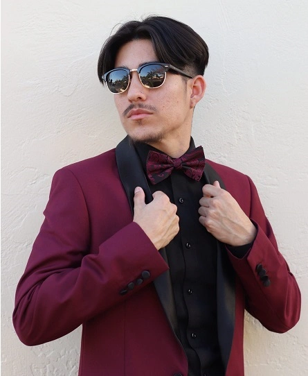 A Model Adjusting A Burgundy Maroon Prom Suit Jacket With Black Lapels And A Matching Bow Tie, Showcasing The 2026 Trend For Photographically Consistent Colors.