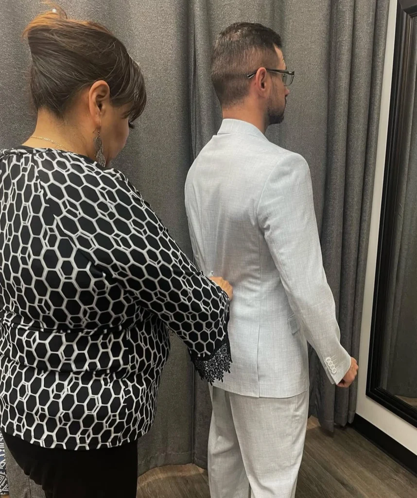 Tailor Checking The Back Drape And Shoulder Fit Of A Light Grey Suit In The Fitting Room