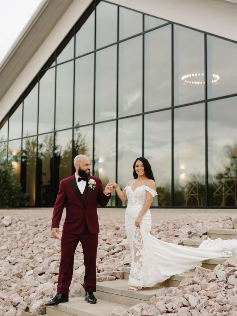 Groom Wearing A Tailored Burgundy Tuxedo With Black Satin Lapels And Bow Tie At A Modern Phoenix Wedding Venue With Desert Landscaping.