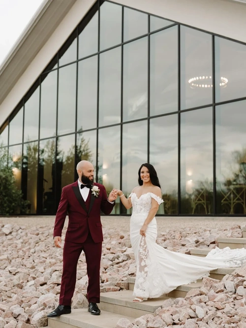 Groom Wearing A Tailored Burgundy Tuxedo With Black Satin Lapels And Bow Tie At A Modern Phoenix Wedding Venue With Desert Landscaping.