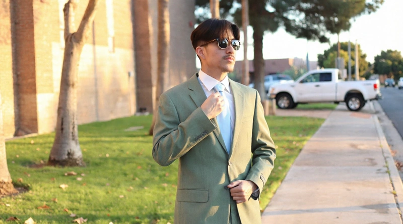 Groom Adjusting A Light Blue Tie On A Sage Green Suit In Phoenix, Styled With A Crisp White Shirt