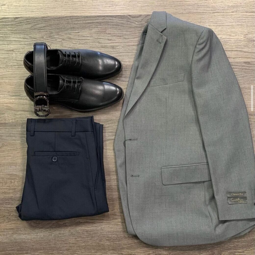A gray suit jacket laid out next to a pair of shoes, folded pants, and a belt