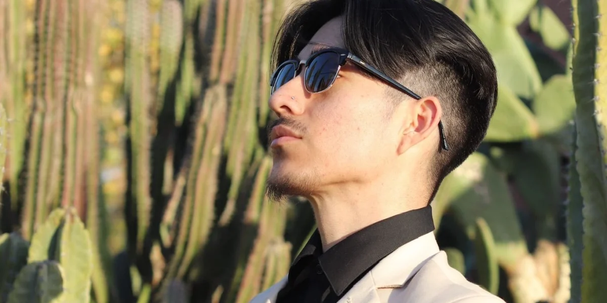 Close up of a man wearing a beige suit with a black shirt and sunglasses in front of desert cacti in Phoenix.