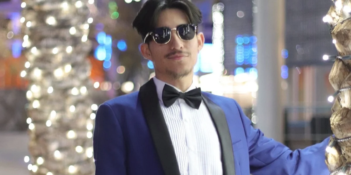 Man wearing a navy blue tuxedo with black bow tie and satin lapels standing next to palm trees with string lights at an evening event in Phoenix.